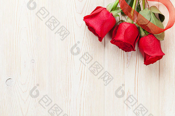 木桌上放着红玫瑰。情人节背景。具有空间的俯视图