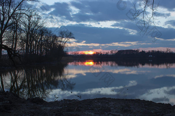 湖面上美丽的日落。夕阳照亮的云彩反射在水面上。湖边树木丛生。