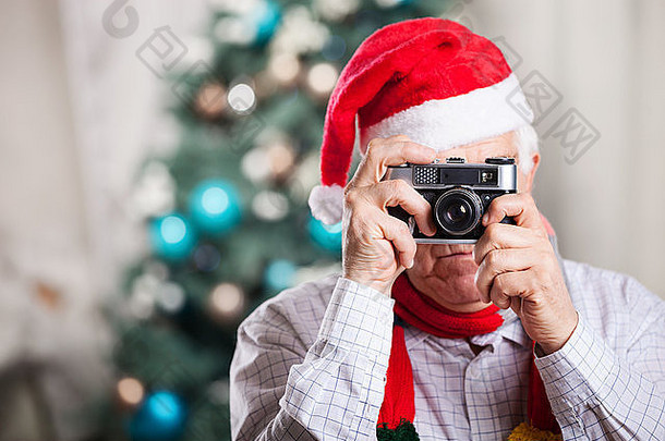 戴圣诞老人帽子的老人在圣诞背景下拍照
