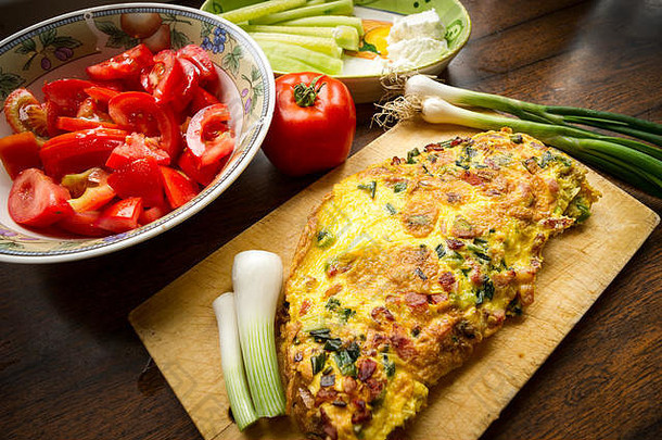 美味的鸡蛋蛋卷配洋葱和烤面包，放在木板上，配番茄沙拉、一个番茄、黄瓜、白奶酪和调味品