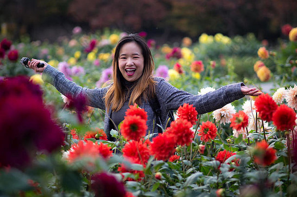 日本花园里，一位美丽的女子在红花旁摆姿势