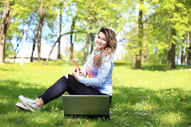 年轻漂亮的女孩在户外用笔记本电脑工作，躺在草地上，白人20岁