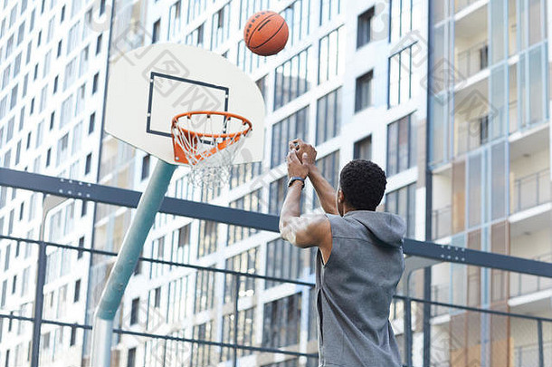 城市背景下，非洲男子在室外篮球场投篮扣篮的后视图，空间