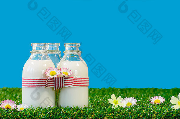 蓝天下的草地上放着三小瓶牛奶