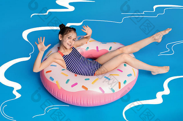 快乐的小女孩在甜甜圈形状的粉色充气戒指上放松
