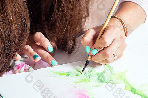 特写一位深色头发、指甲明亮的艺术家在<strong>画册</strong>中用薄木笔和水彩画了一朵绿叶粉红牡丹