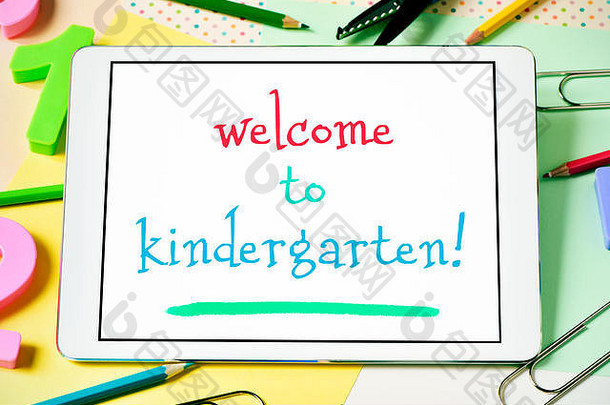 一台平板电脑的特写镜头，屏幕上有“欢迎来到幼儿园”的文字，桌上放满了数字和d字铅笔蜡笔