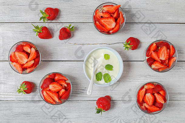 新鲜成熟的有机草莓切成片，放在玻璃罐中，配上的天然酸奶，放在带勺子的白碗中，放在放有草莓的木桌上，