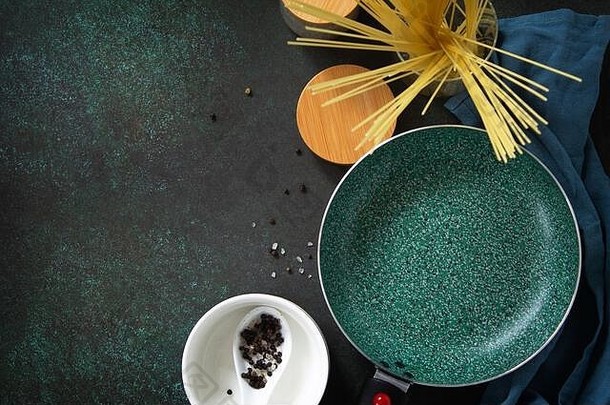 新的空煎锅，陶瓷涂层，放在厨房石桌上，周围是意大利料理配料。俯视平面背景。空间。