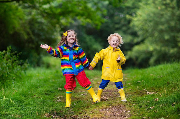 男孩女孩玩多雨的夏天公园孩子们色彩斑斓的彩虹夹克防水靴子跳水坑