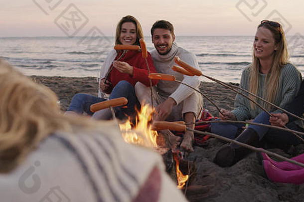 一群年轻朋友深夜坐在火炉旁，烤香肠，喝啤酒，聊天，玩得很开心