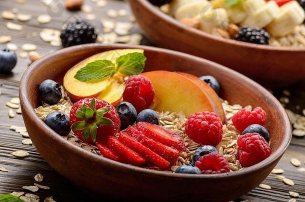 木制厨房餐桌上的粘土盘中有桃子、草莓、杏仁和黑莓等果味健康的慕斯利