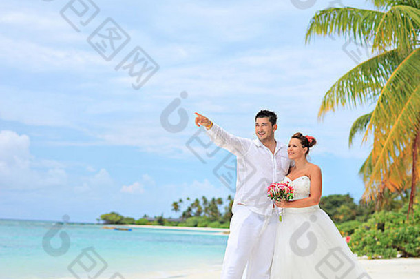 在马尔代夫拉维亚尼环礁的库雷杜岛上，一名新娘手持花束，新郎朝前看