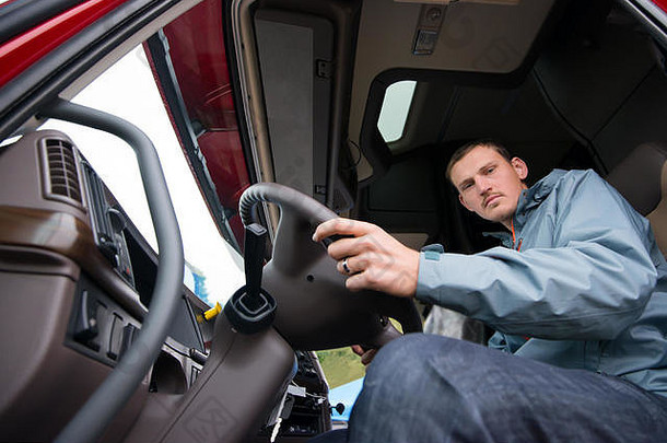 一位年轻的卡车司机驾驶着现代化舒适的驾驶室，驾驶着一辆大卡车，驾驶室很高，打开车门准备开始行驶