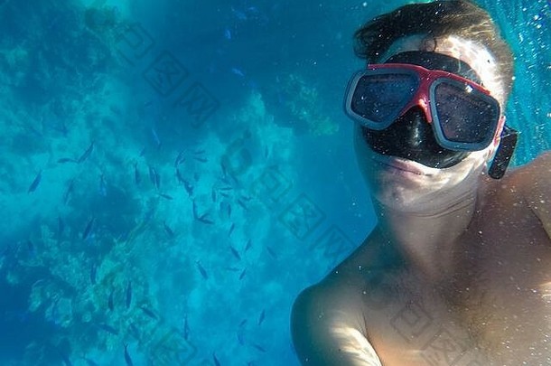 一名戴着水下面具的男子在红海珊瑚附近游泳，从事潜水