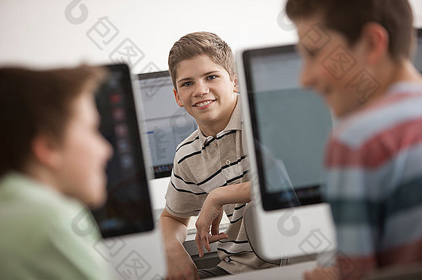 有一排计算机显示器和座位的教室计算机实验室。三个年轻人在一起聊天。