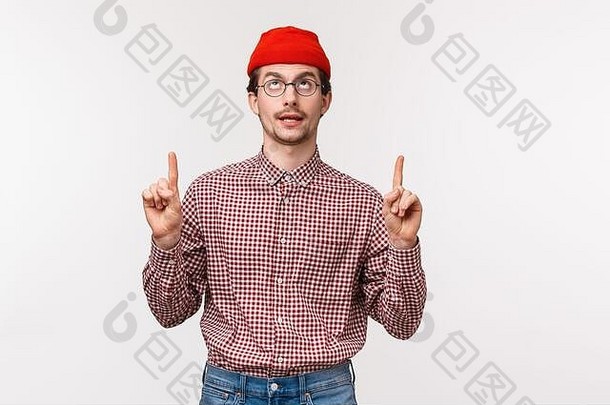 腰身向上的肖像有趣、富有创意的年轻人，戴着眼镜，戴着红色的帽子，手指朝上，眼睛向上转动，好像看到了什么
