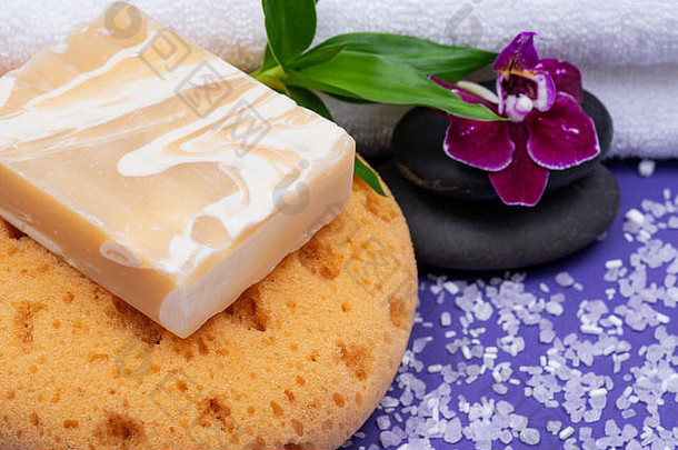 Spa健康概念。天然泡沫沐浴海绵、杏仁山羊奶皂、玄武岩石材、紫色背景上的竹子和兰花。