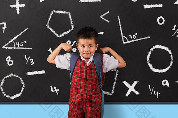 穿着校服的小男孩在黑板前伸展肌肉。