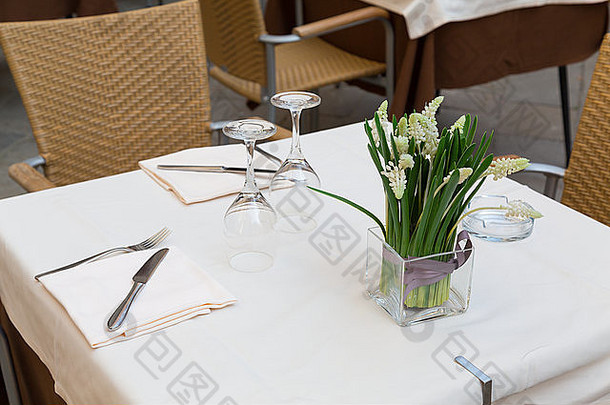 威尼斯一家餐馆的一张桌子的一部分的特写，展示桌子、餐具、眼镜、椅子和鲜花
