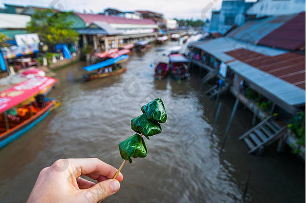泰国安法瓦浮动市场的水渠上方，用棍子将明康包裹在泰国食物上