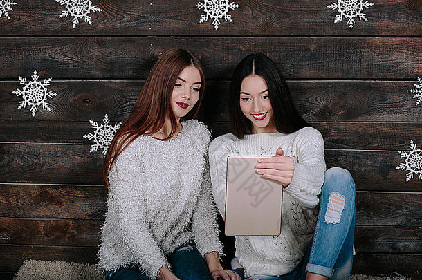 两个漂亮的女孩拿着一块平板电脑，在礼物之间