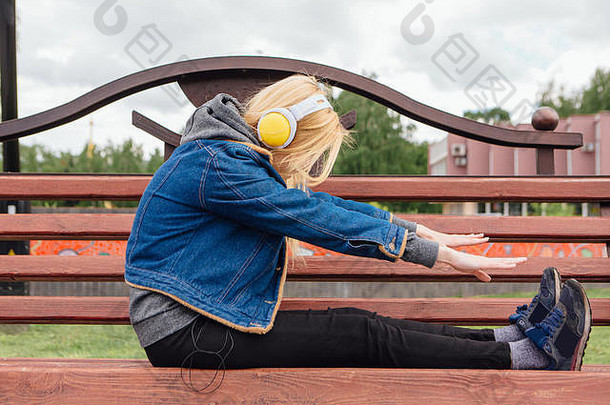 坐在长椅上戴着耳机听音乐的女孩