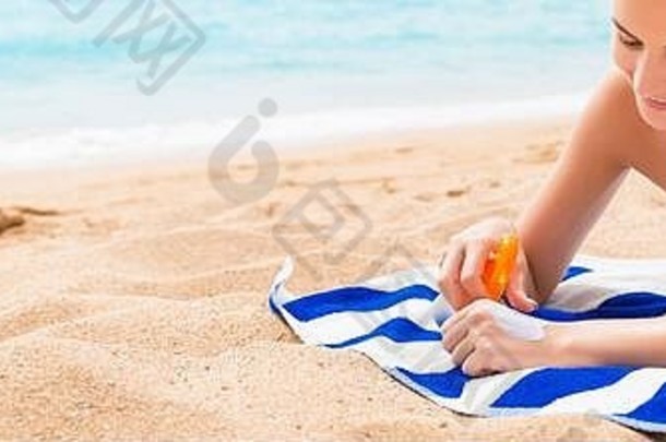 年轻快乐的女人在海边的<strong>毛巾</strong>上休息，用防晒霜保护手上的皮肤不受喷雾的伤害。