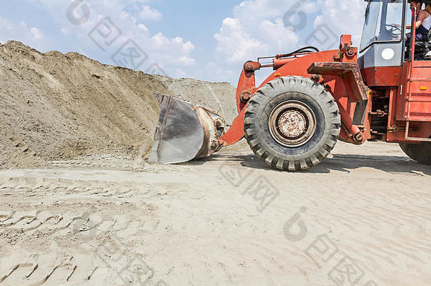 土方工程中带轮子的红色装载机。推土机正在把沙子推到巨大的桩上。