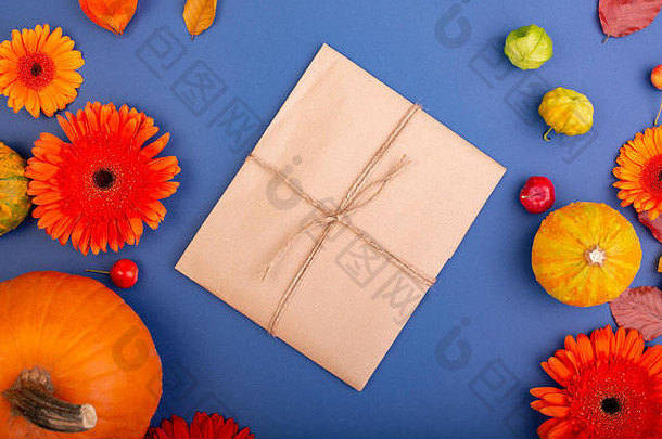 手工礼品盒的俯视图，蓝色背景上有黄色和橙色的花朵和南瓜。空白贺卡的创意工作设计。平铺。