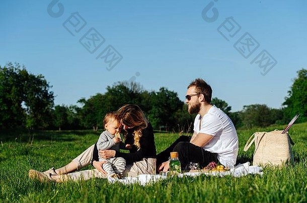 野餐时，一家人在毯子上休息，给婴儿喂脆面包