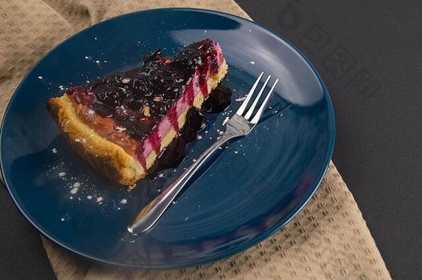 黑色的桌子上放着蓝莓<strong>慕斯</strong>蛋糕，蓝色盘子上有镜面釉装饰的浆果和薄荷叶。俯视图