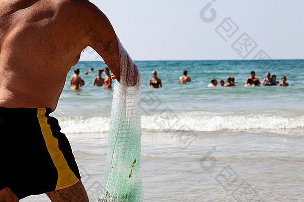 以色列特拉维夫——2012年8月18日：一名成年男子在炎热的夏日从海滩上拔出渔网。