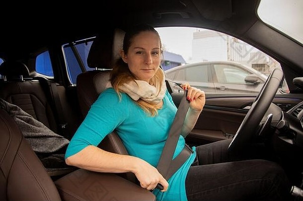 <strong>驾驶</strong>安全概念。一位年轻的女司机坐在一辆现代化的汽车里，系上安全带。女<strong>人</strong>微笑着看着相机。特写镜头，柔和的