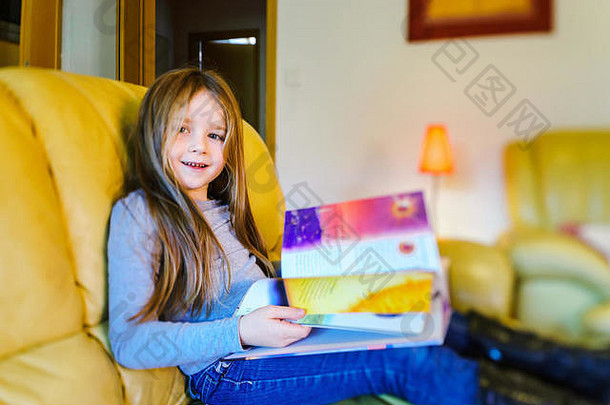 可爱的长发小女孩在livivng room阅读儿童读物，倾斜视角