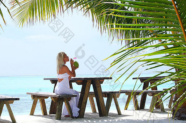 坐在棕榈树、天空和大海背景下的热带咖啡馆里的女人