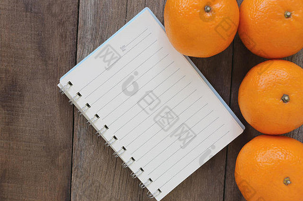 笔记本和橘子放在旧木地板上，设计理念是关于健康食品。