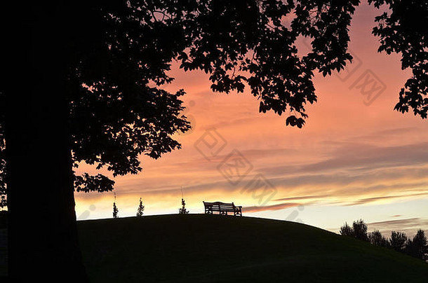 空荡荡的公园座位和树木在落日的橙色余晖衬托下形成了一幅宁静<strong>祥和</strong>的景象。
