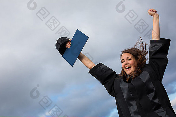 美丽的年轻女子欢庆她的毕业典礼——张开双臂，拿着毕业证书，品味她的成功