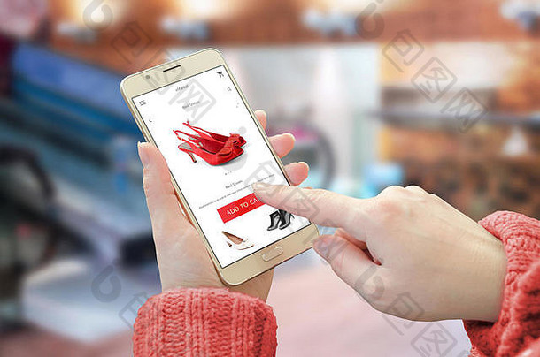 智能手机上的购物网站应用程序。拿着移动设备买红鞋的女人。背景为城市购物中心。
