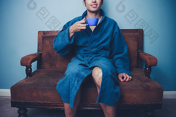 穿着浴衣在沙发上喝咖啡的年轻人