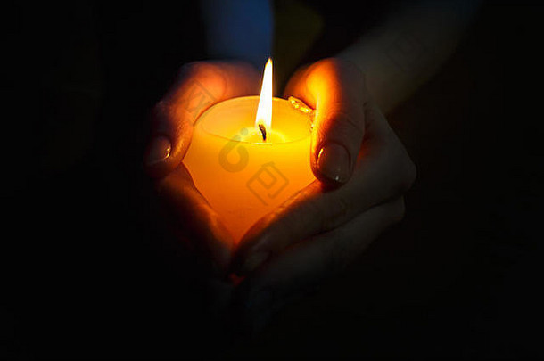 在黑色背景下，一个祈祷的女孩手中点燃蜡烛