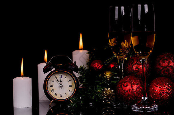 两个酒杯，配香槟、时钟、蜡烛和圣诞装饰品，背景为黑色，带有反光。空间。圣诞快乐，新年快乐