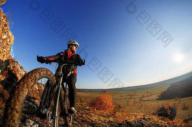 骑自行车的人站在明亮的太阳和蓝天下的低角度视图。