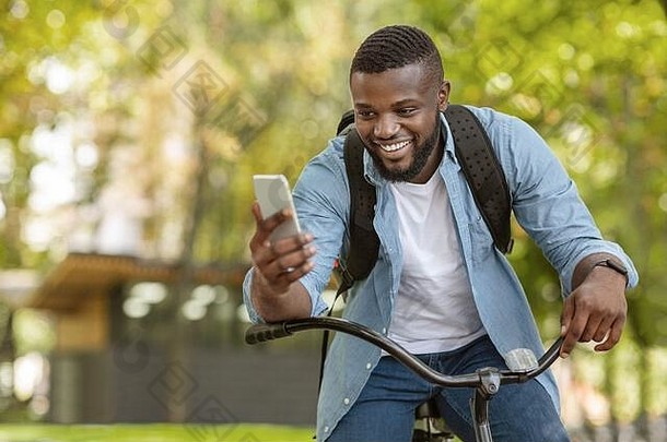 快乐黑色的男人。骑自行车在户外智能手机