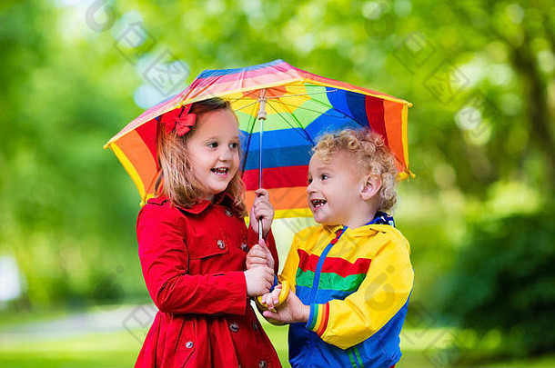 小男孩和小女孩在雨中的公园里玩耍。孩子们带着五颜六色的彩虹伞、防水夹克和外套在雨中玩耍