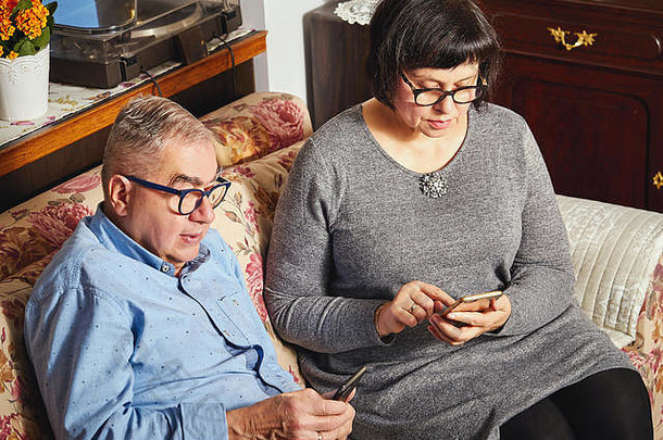 结婚老年夫妇坐在家里的沙发上用手机上网。