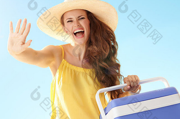 微笑活跃的女人色彩鲜艳的衣服蓝色的塑料冷却器盒子挥臂蓝色的天空