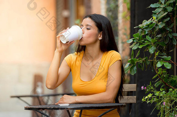 一位20多岁的迷人拉丁女人坐在<strong>咖啡</strong>馆外快乐地喝着<strong>咖啡</strong>