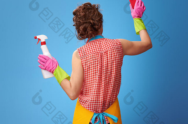 大扫除时间。从后面看，年轻女子穿着黄色围裙，用厨房海绵清洁，蓝色隔离